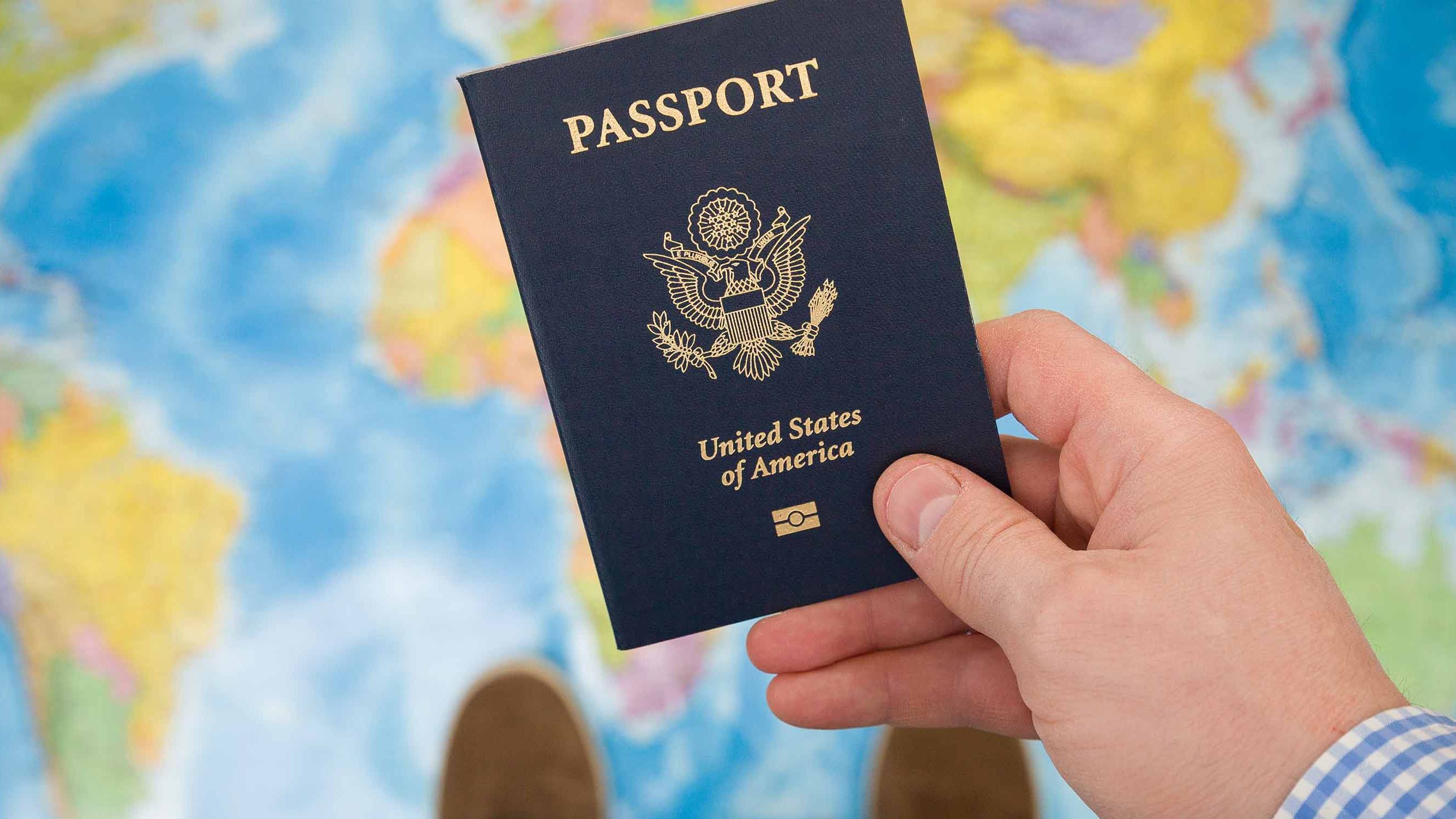 picture of a man holding a U.S. passport while standing on a map of the world