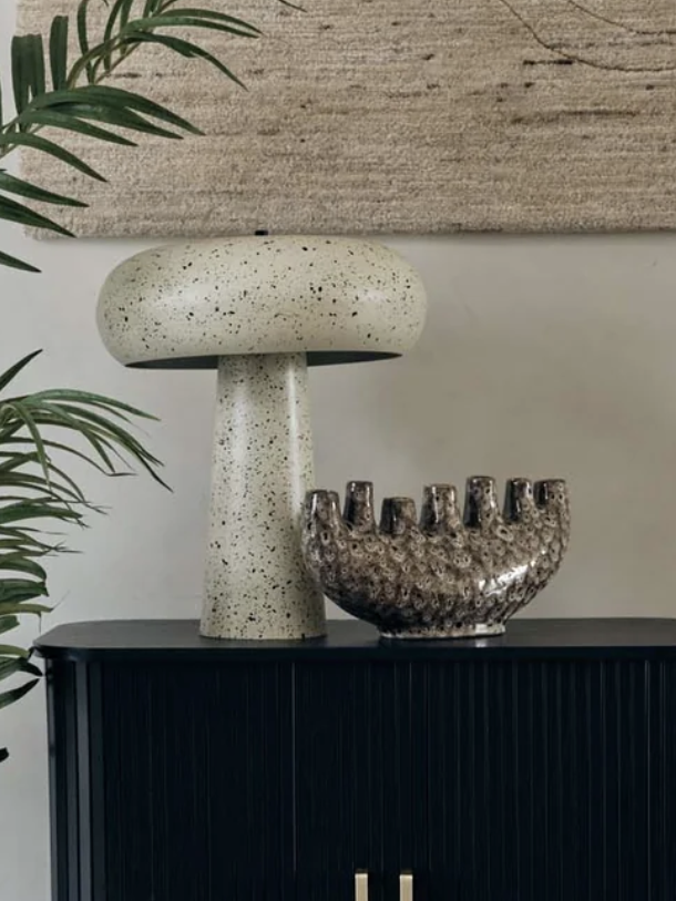 Metal table lamp on a black cabinet with a palm plant beside it
