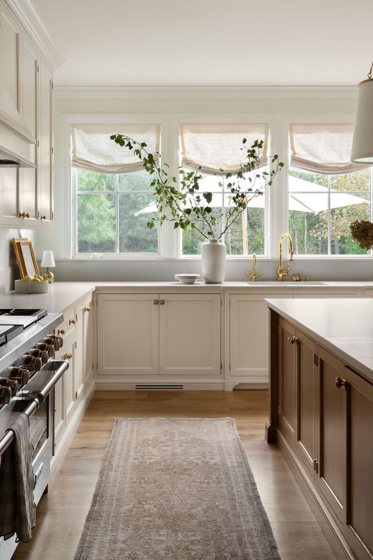 A warm neutral kitchen with off-white cabinets, gray countertops, a wooden island, and sheer linen fabric blinds over the windows