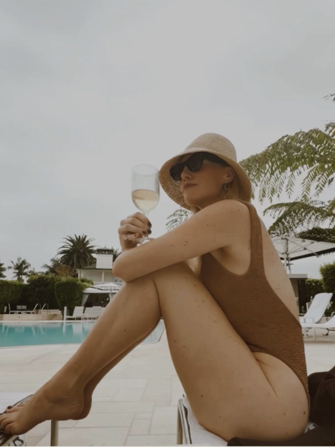 Brooke Ely Danielson wears a cloche sunhat with a brown one-piece swimsuit