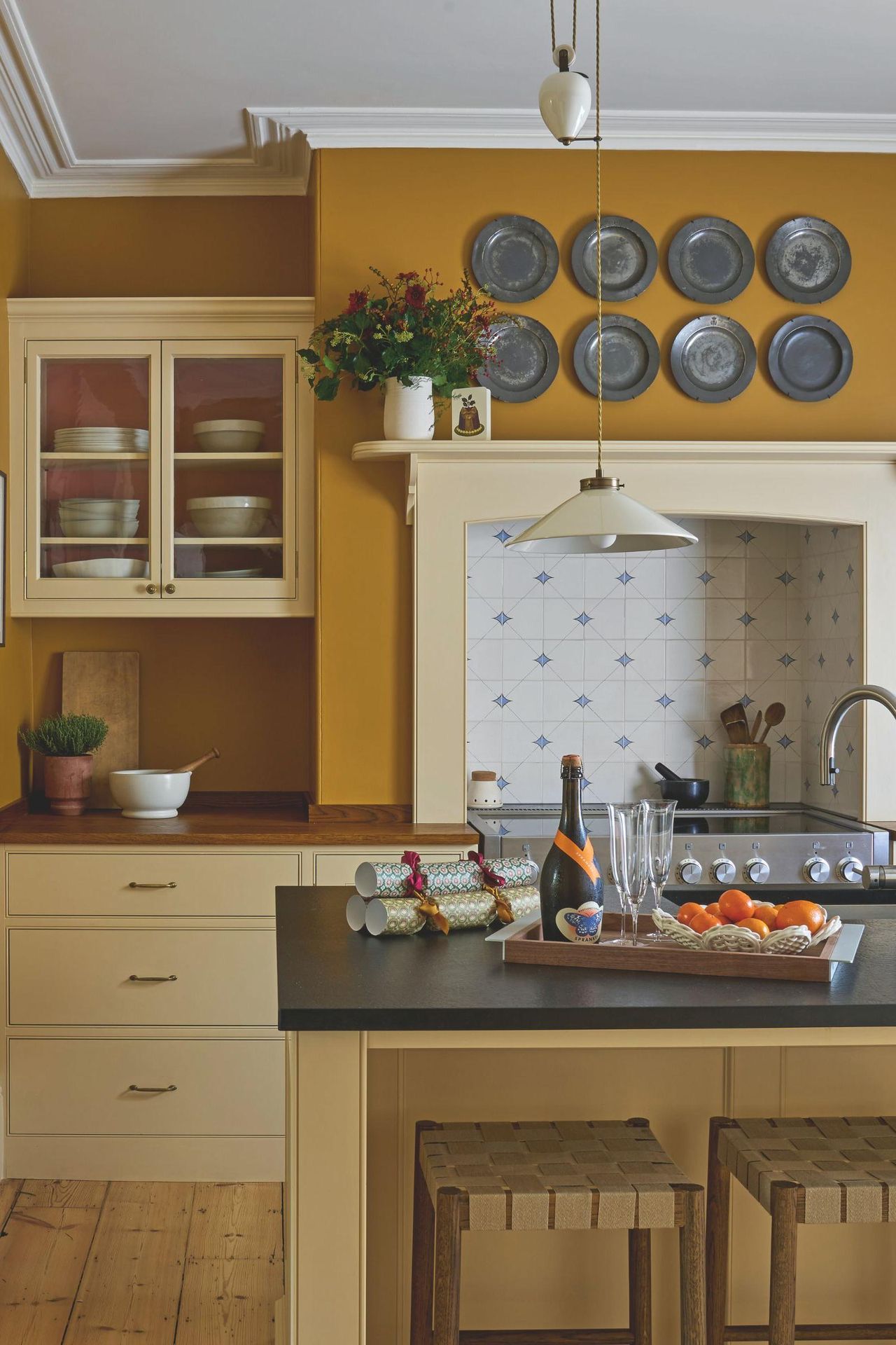 Yellow kitchen with dark yellow walls and lighter cabinetry. There is an island in the middle and a range with delft tiles