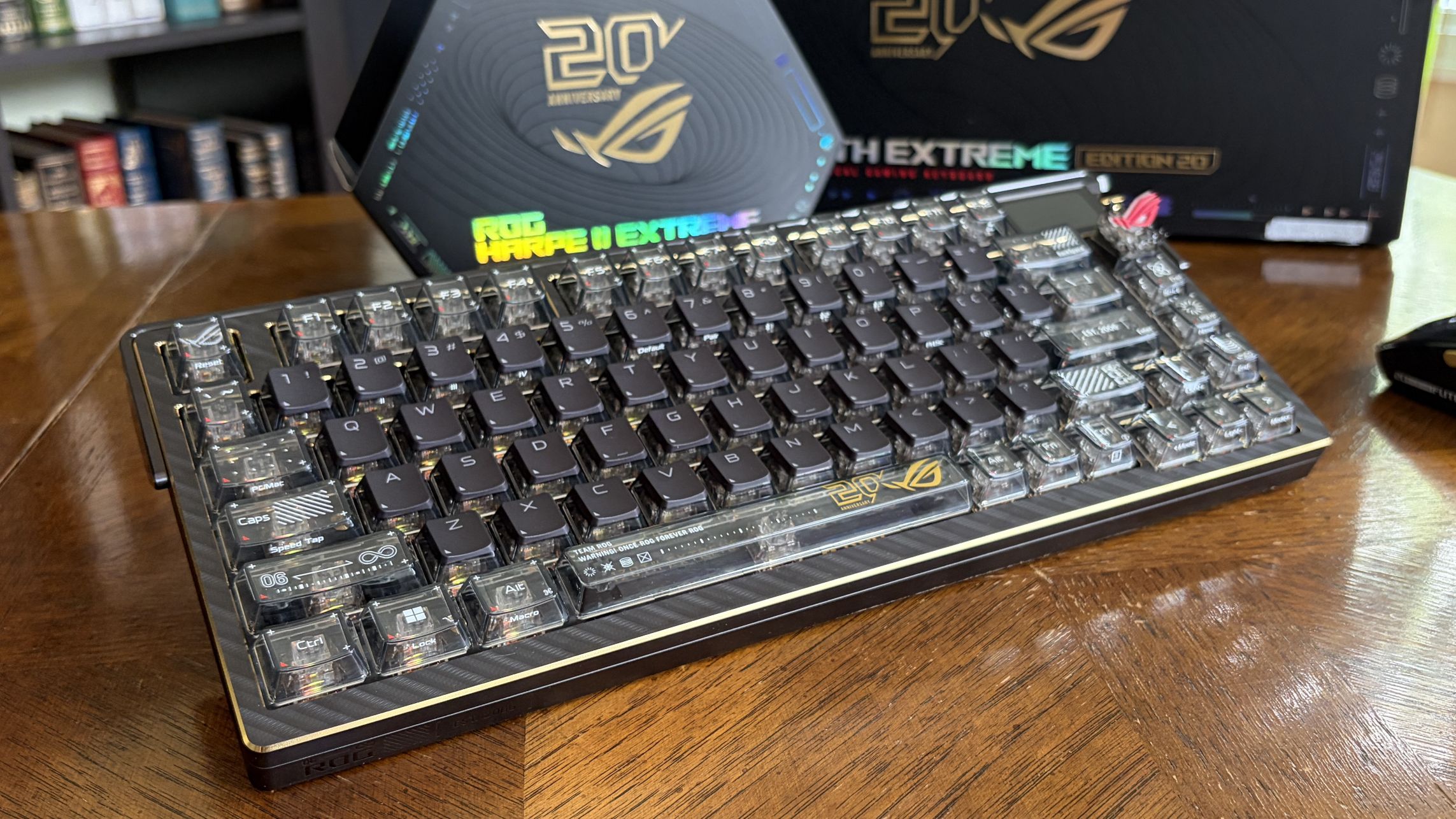 ASUS ROG mechanical keyboard and wireless mouse on a wooden table, with ROG-branded boxes in the background.