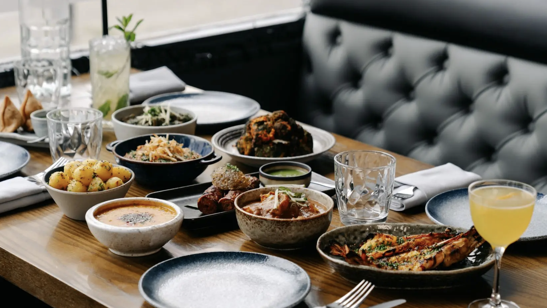 an image of a ready laid table at Koyal with nine different small dishes across it, as well as two different cocktails