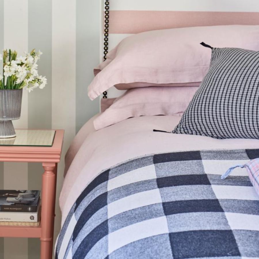 Bedroom with pale blue and white striped wallpaper, blue checked throw, pink pillows, and pink and white cushions