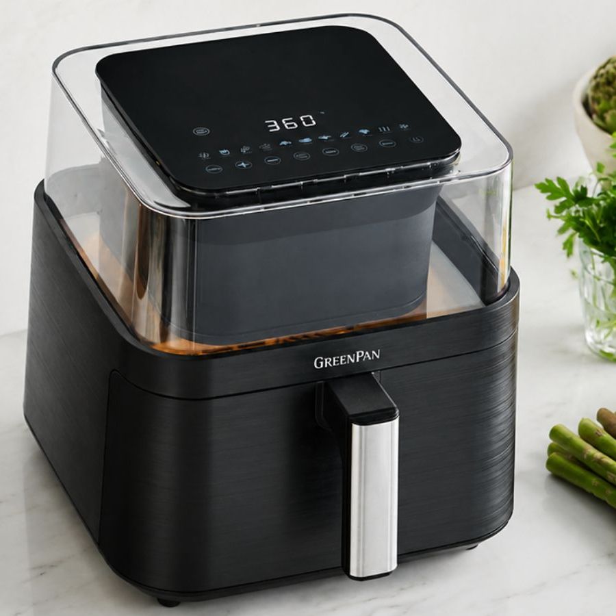 The GreenPan Bistro 360 Clear View Air Fryer on a marble kitchen counter beside a crock of wooden utensils and some fresh spring veg.