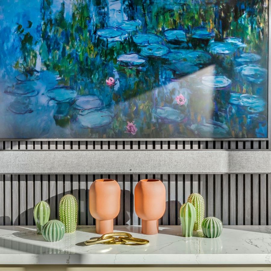 Soundbar and TV showing watercolor art mounted on paneled wall, above marble surface with artificial cacti and pots.