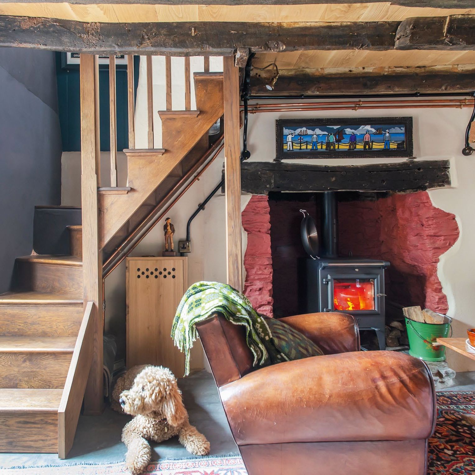 view towards log burner in cottage living room, with exposed ceiling beams and wooden staircase to the side