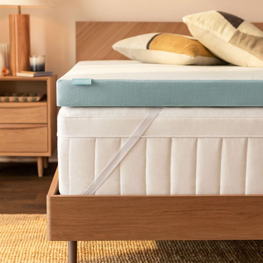 Tempur-Pedic mattress topper om a bed; to the left, a lamp on a wooden nightstand against cream walls.