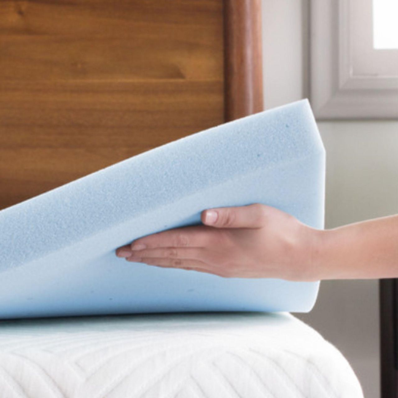 Hand holding up a Lucid mattress topper on the corner of a bed