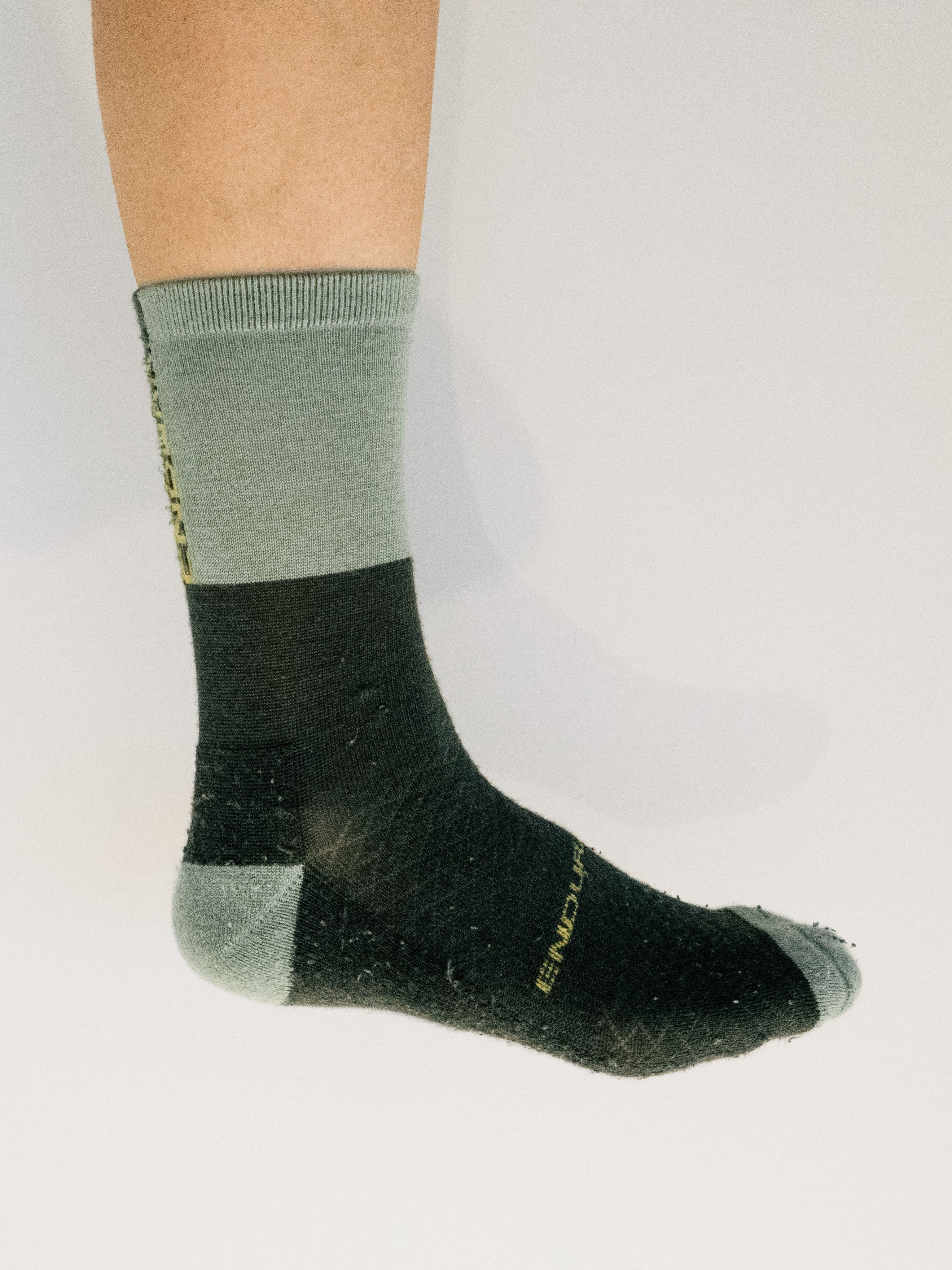 A white leg wears a two-tone green cycling sock against a white background