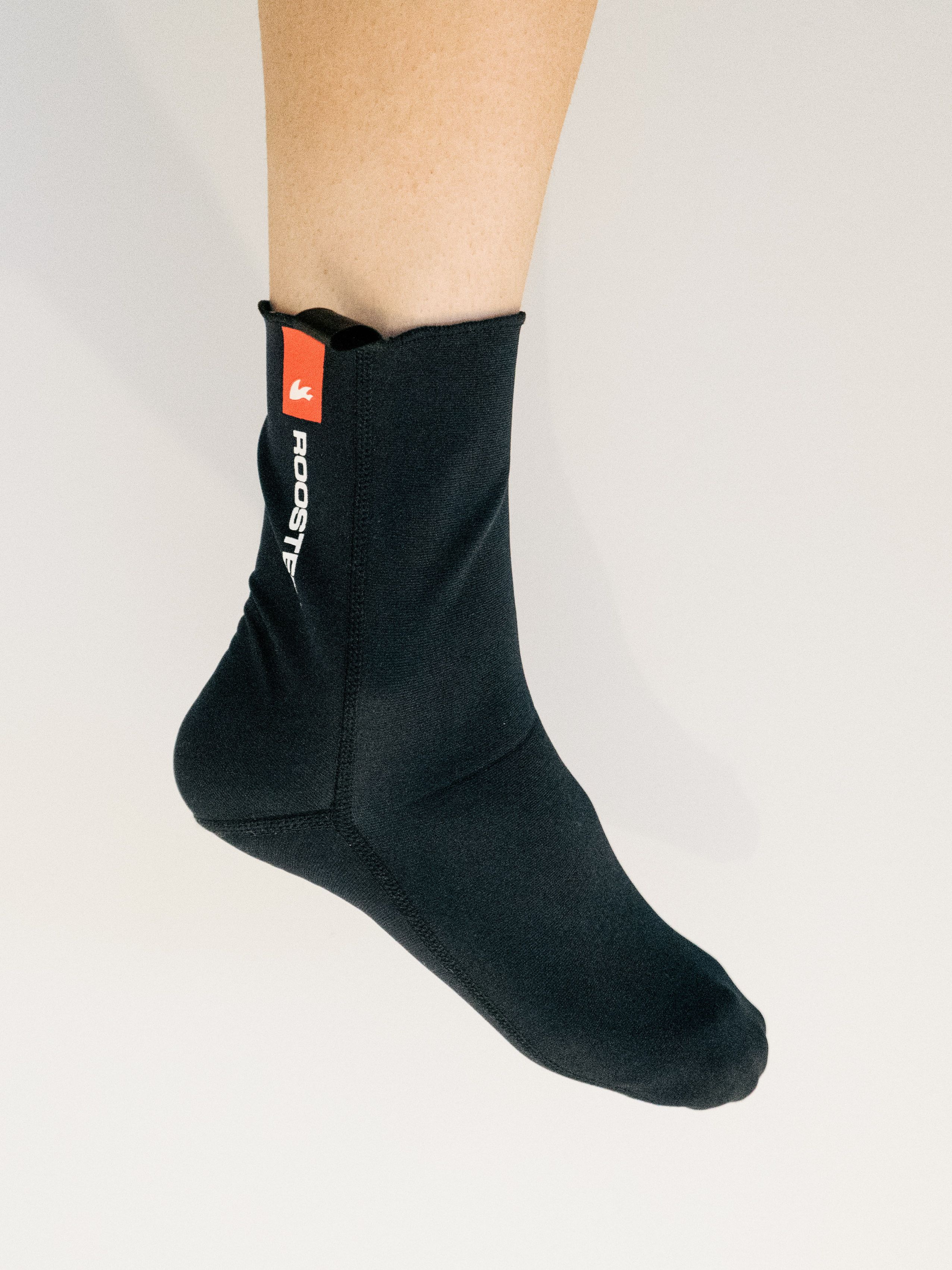 A white leg wears a black neoprene cycling sock against a white background