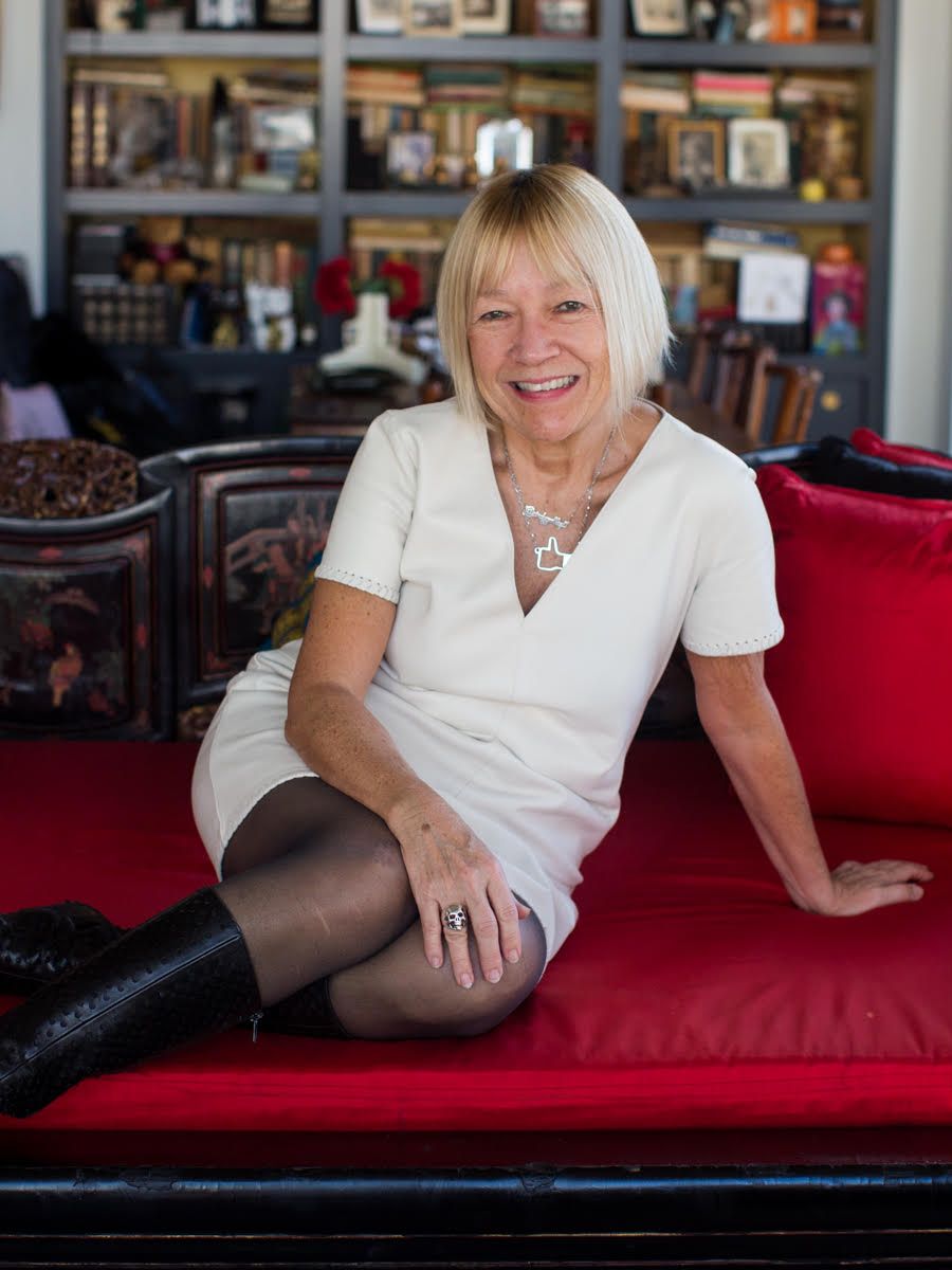 A woman sitting smiling on a red sofa wearing a white dress and black boots