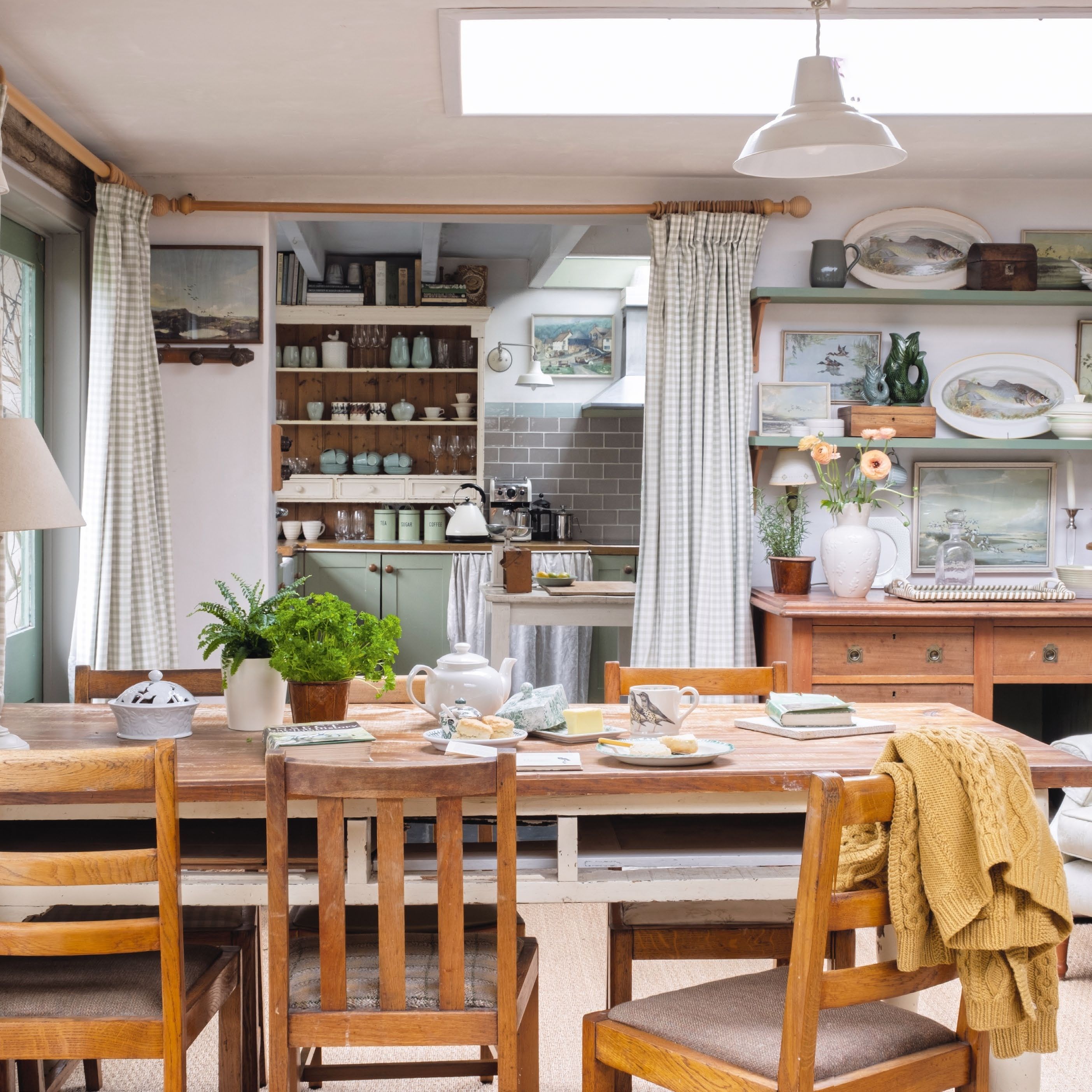 Garden room in cottage decorated in tones of green and blue, with dining table and chairs, leading through to kitchen