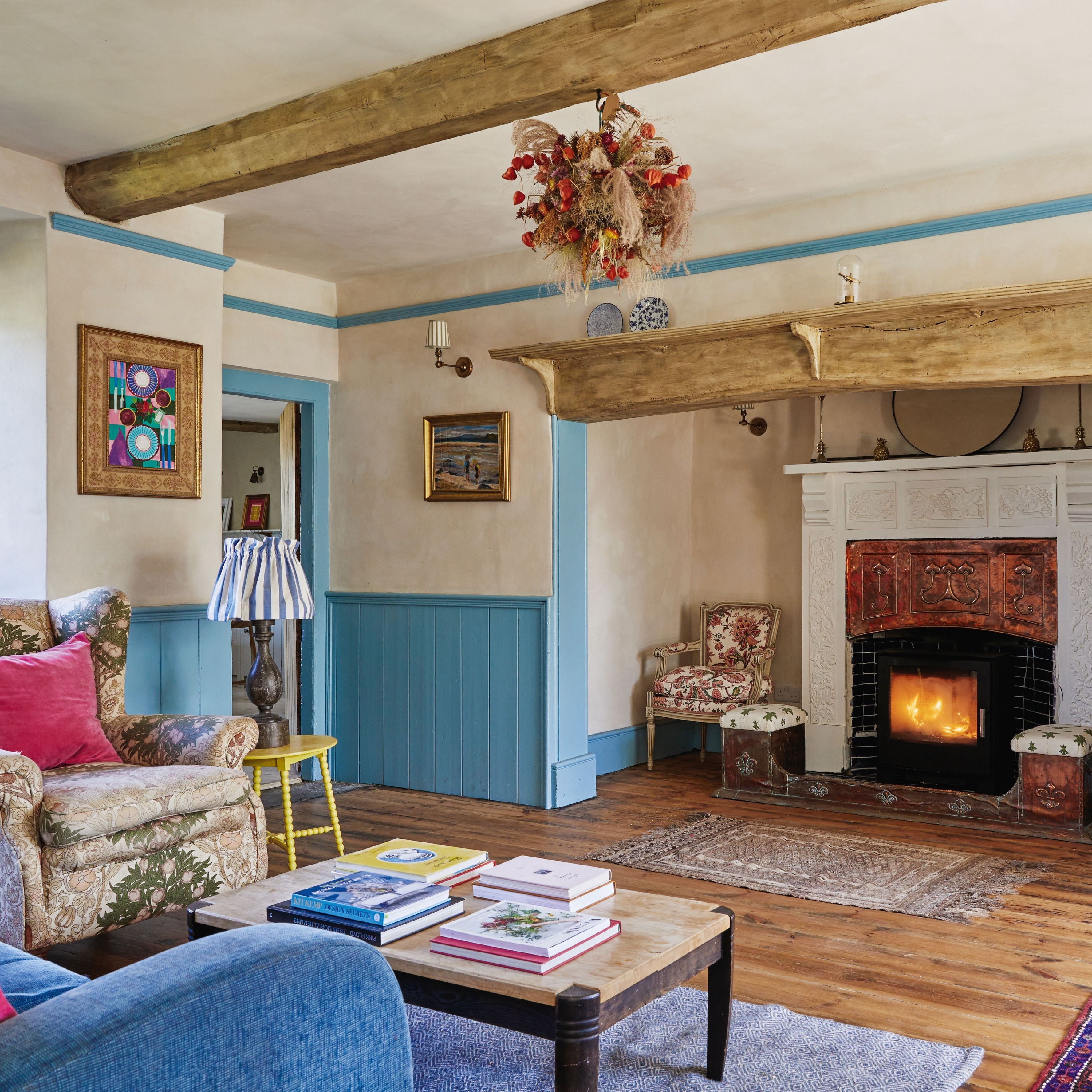 Country living room with log burner in large inglenook, blue painted wall pannelling and woodwork, wooden floors and a mix of old and new furnishings