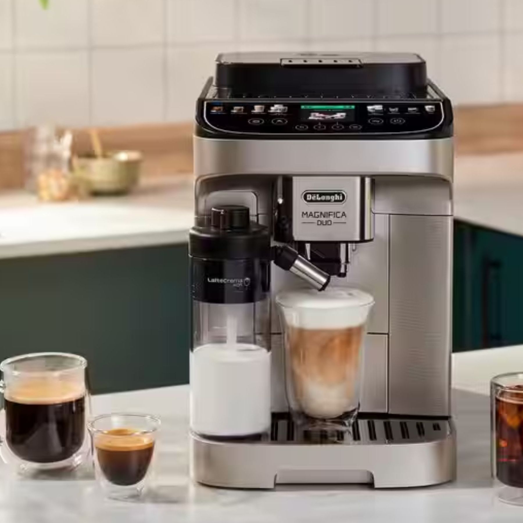 A De'Longhi coffee machine in black and stainless steel with a glass of iced coffee on the drip tray beside an automatic milk dispenser.
