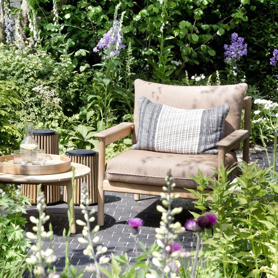Packed flower beds around a paved seating area with a two chairs and a table