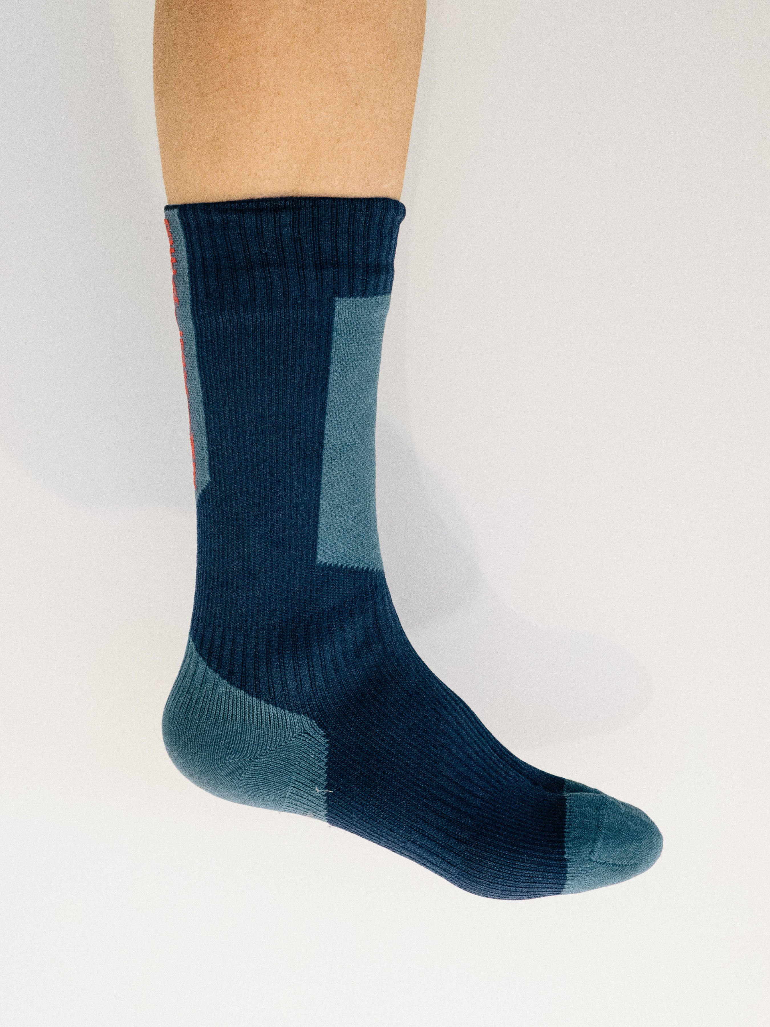 A white leg wears a blue cycling sock against a white background
