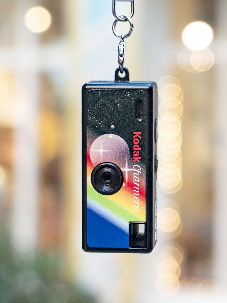 Kodak Charmera compact camera dangling from its keychain, with shop frontage backdrop