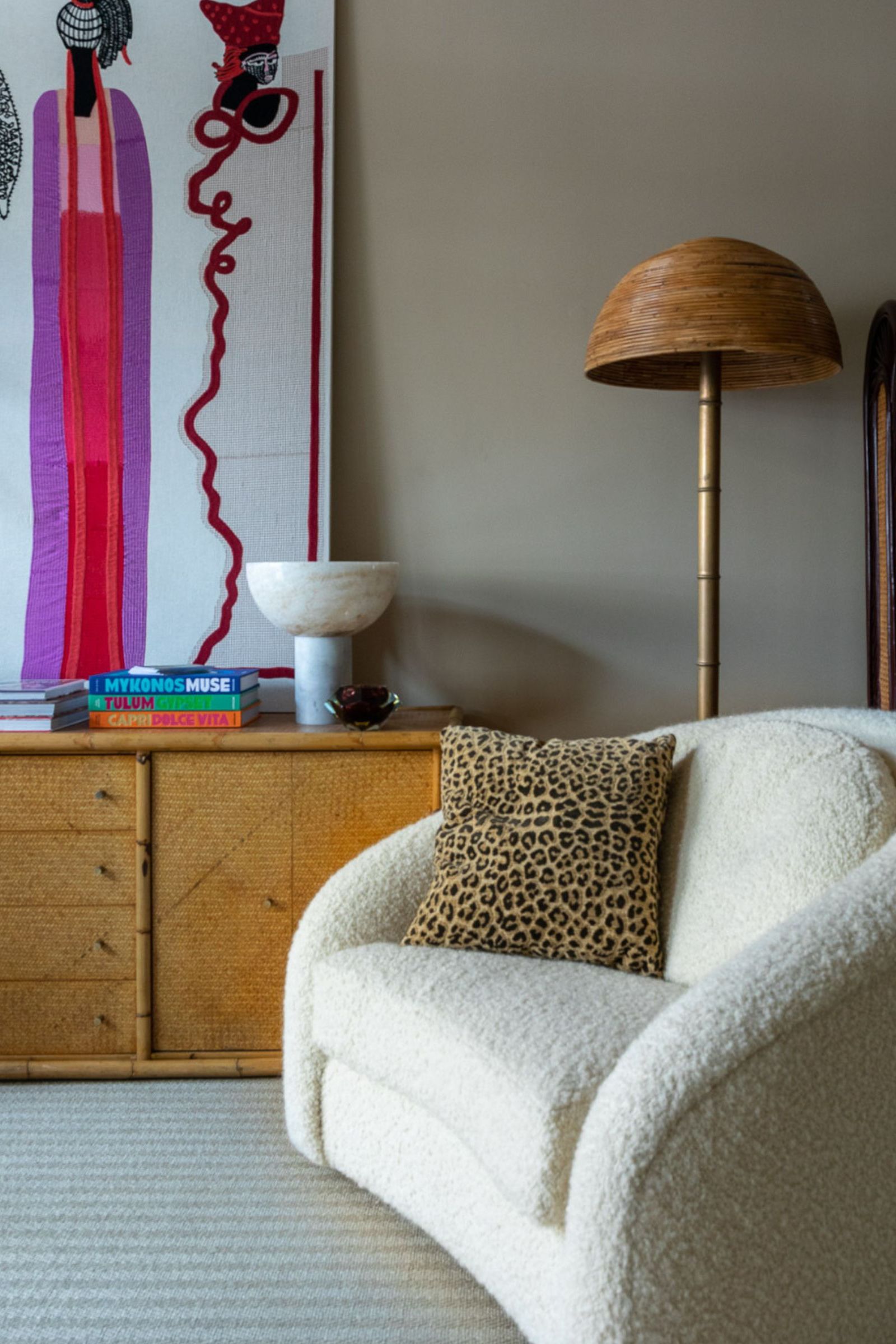 boucle chair next to a wooden sideboard filled with large art and a rattan floor lamp