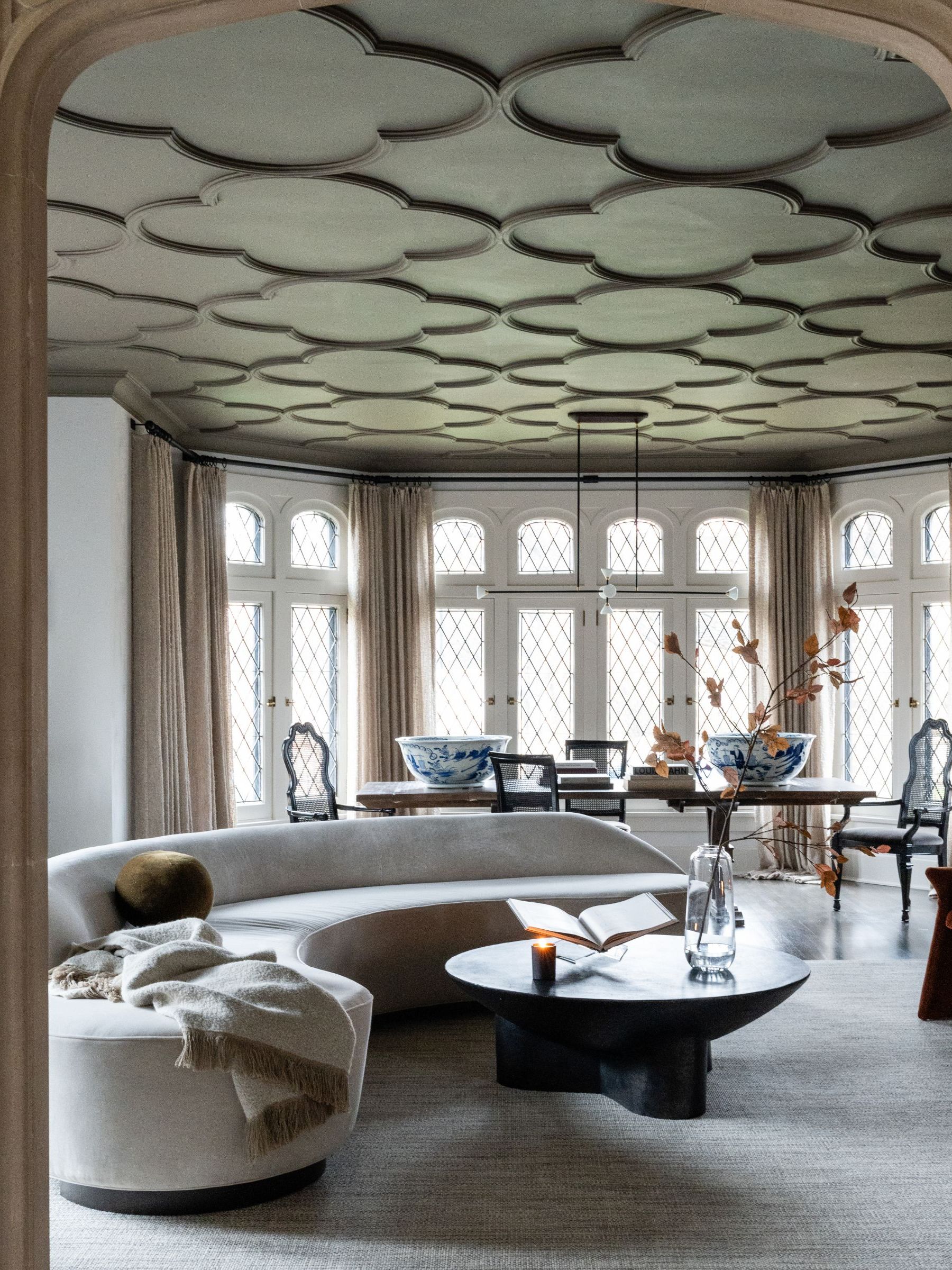 Gothic living room with ornate windows and ceiling, curved boucle sofa and long dining table with blue and white china
