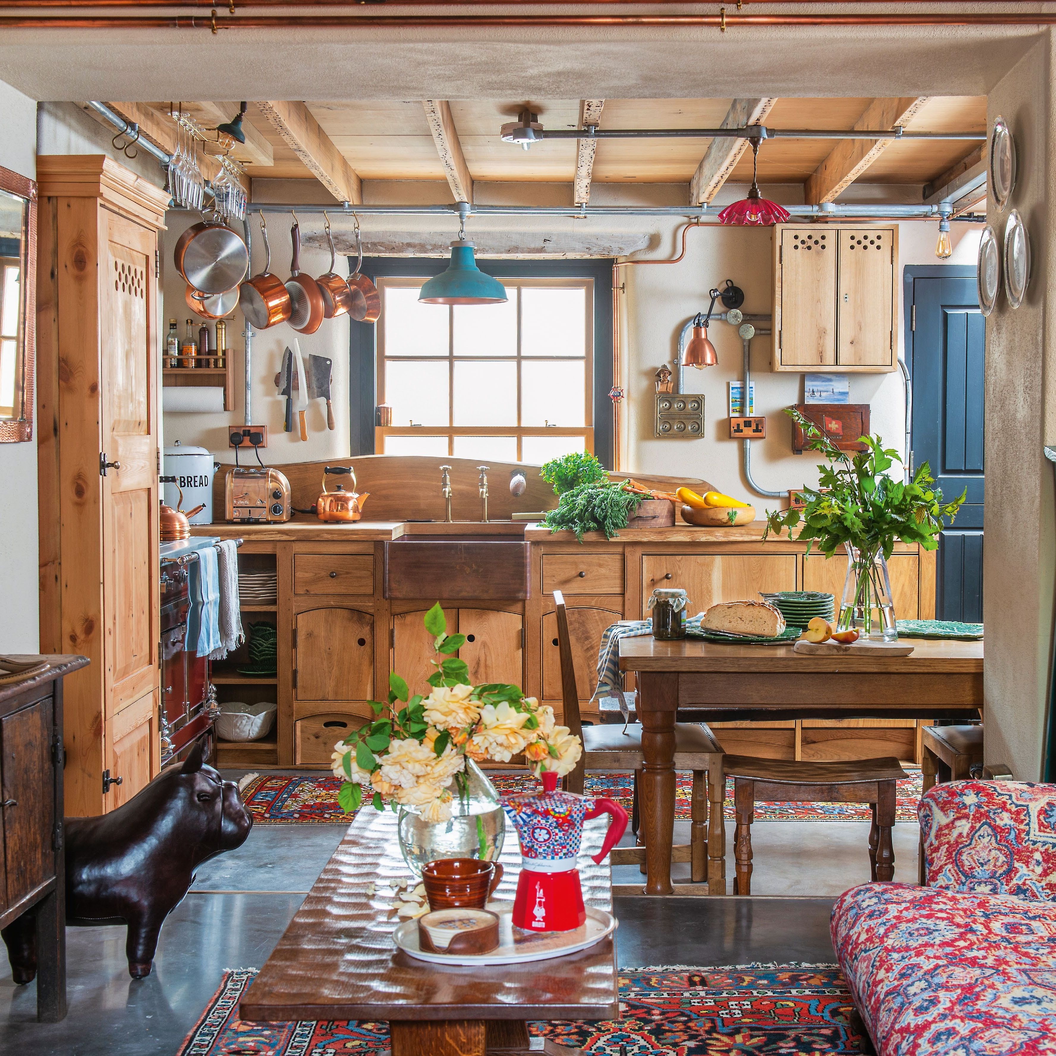 view through to a wooden handmade kitchen in a rustic cottage with exposed ceiling beams and pipework