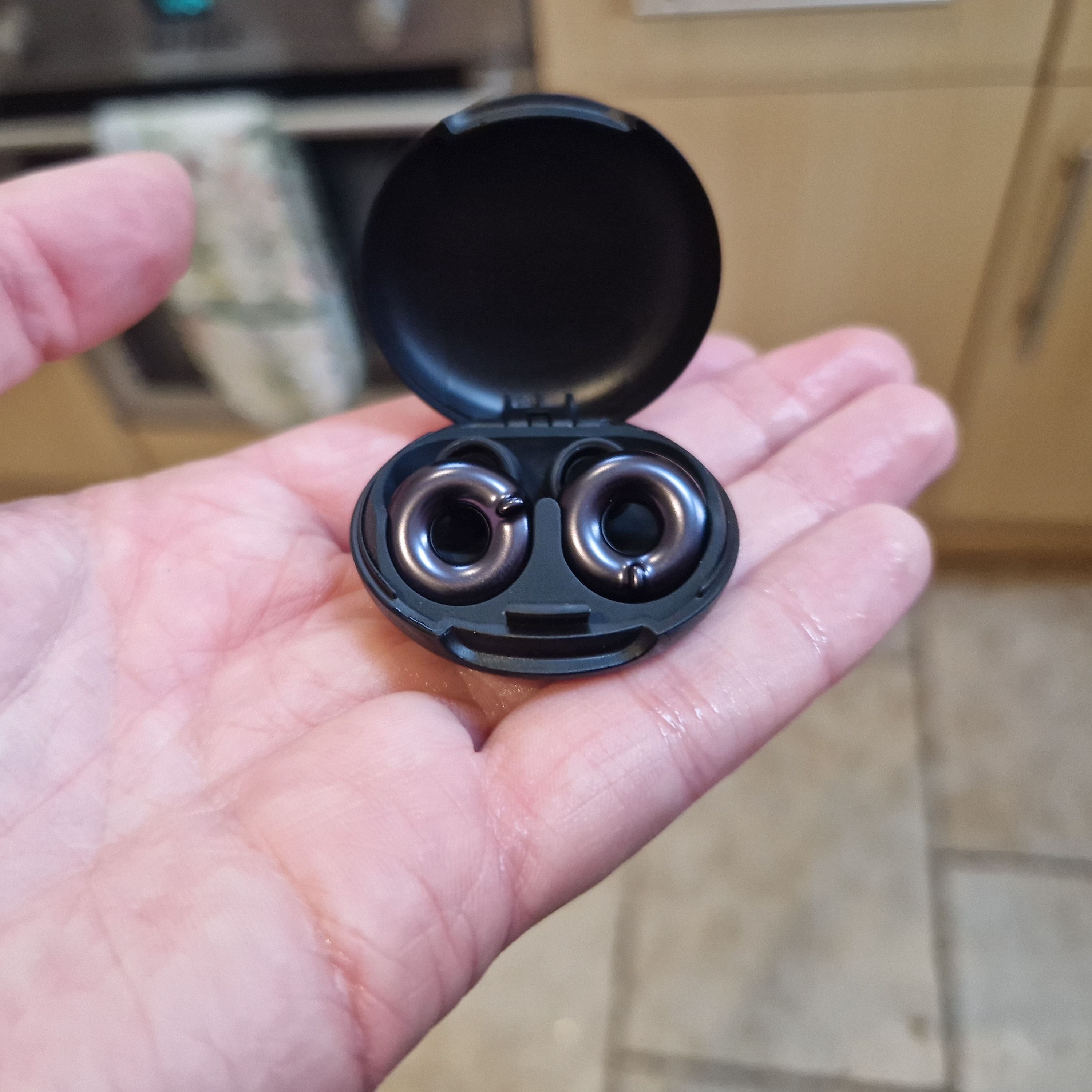 Black earbuds in an open case in someone’s palm
