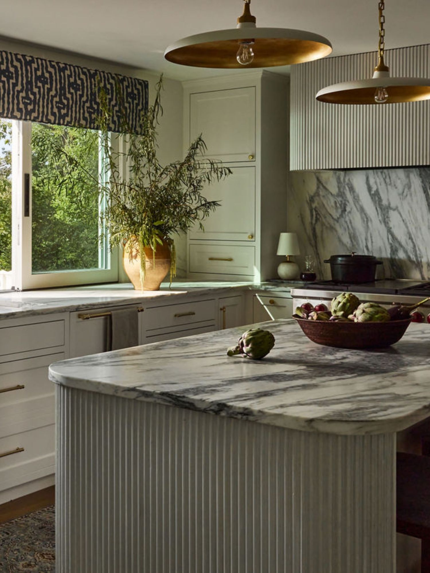 A warm neutral kitchen with marble countertops and a concrete island and range hood