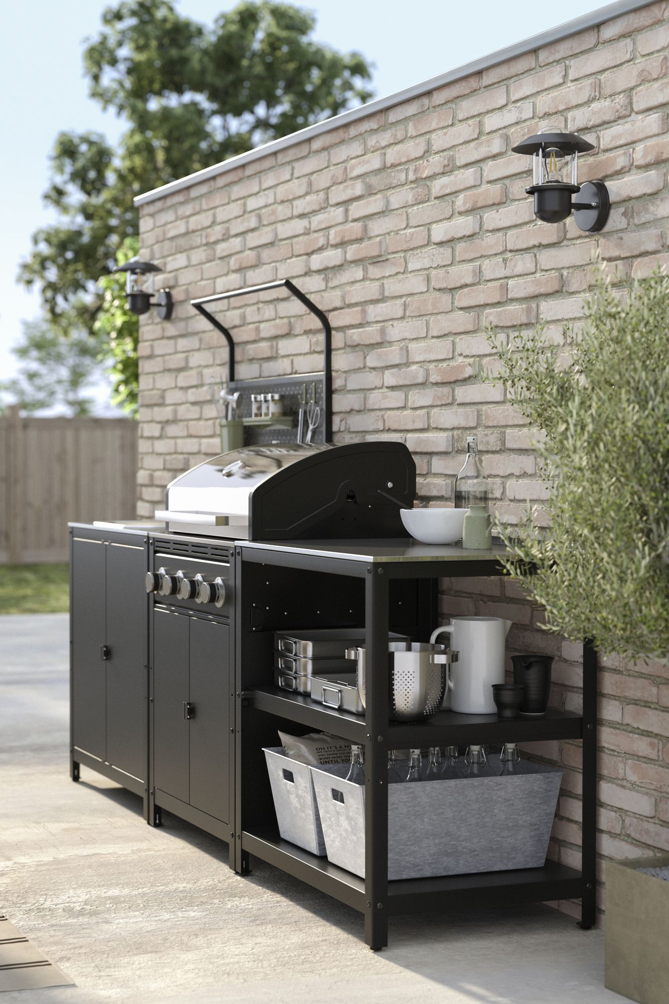 An outdoor kitchen/grill in a dark gray color. There is a concrete patio and the grill space is against a light brick wall. There are green rope dining chairs and part of a black umbrella in view.