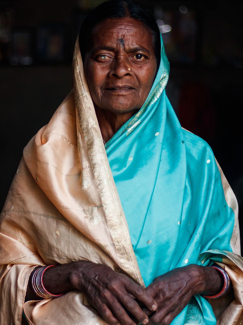 A woman in a tan and blue sari looks at the camera.