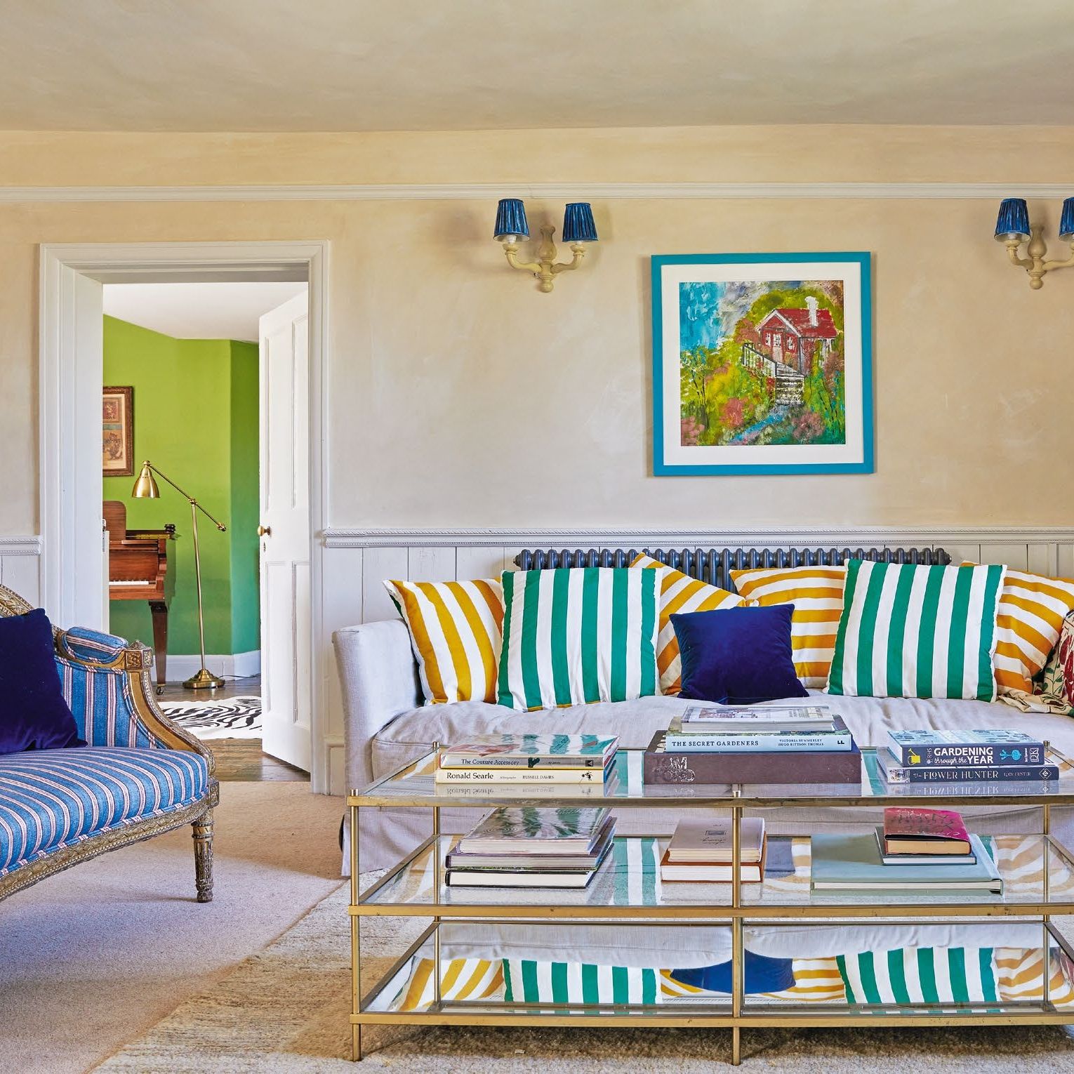 Living room with neutral limewashed walls, antique and new sofas with striped cushions, metal and glass coffee table