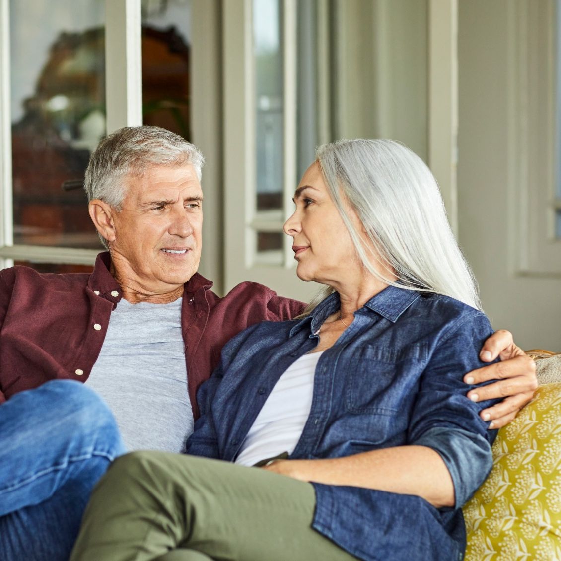 Mature good looking couple talking while sitting on sofa at home