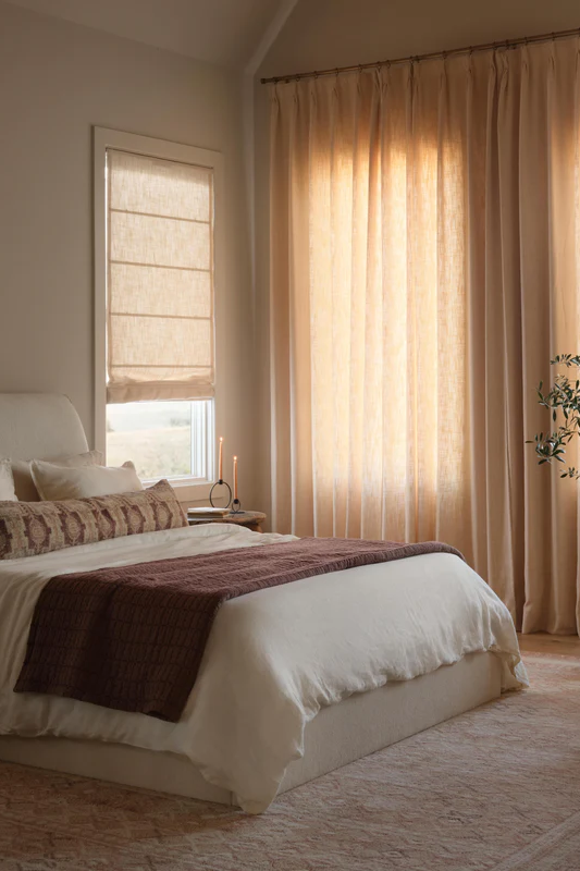Minimalist bedroom dressed with sheer curtains and warm, neutral bedding blending terracota and cream.