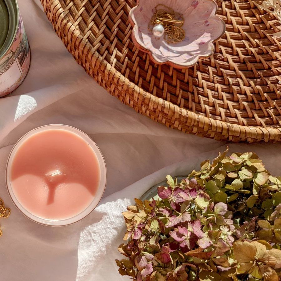 top down image of a pink, unburnt candle beside a jar of matches on its side, a can, a woven tray, and some dried hydrangea flowers.