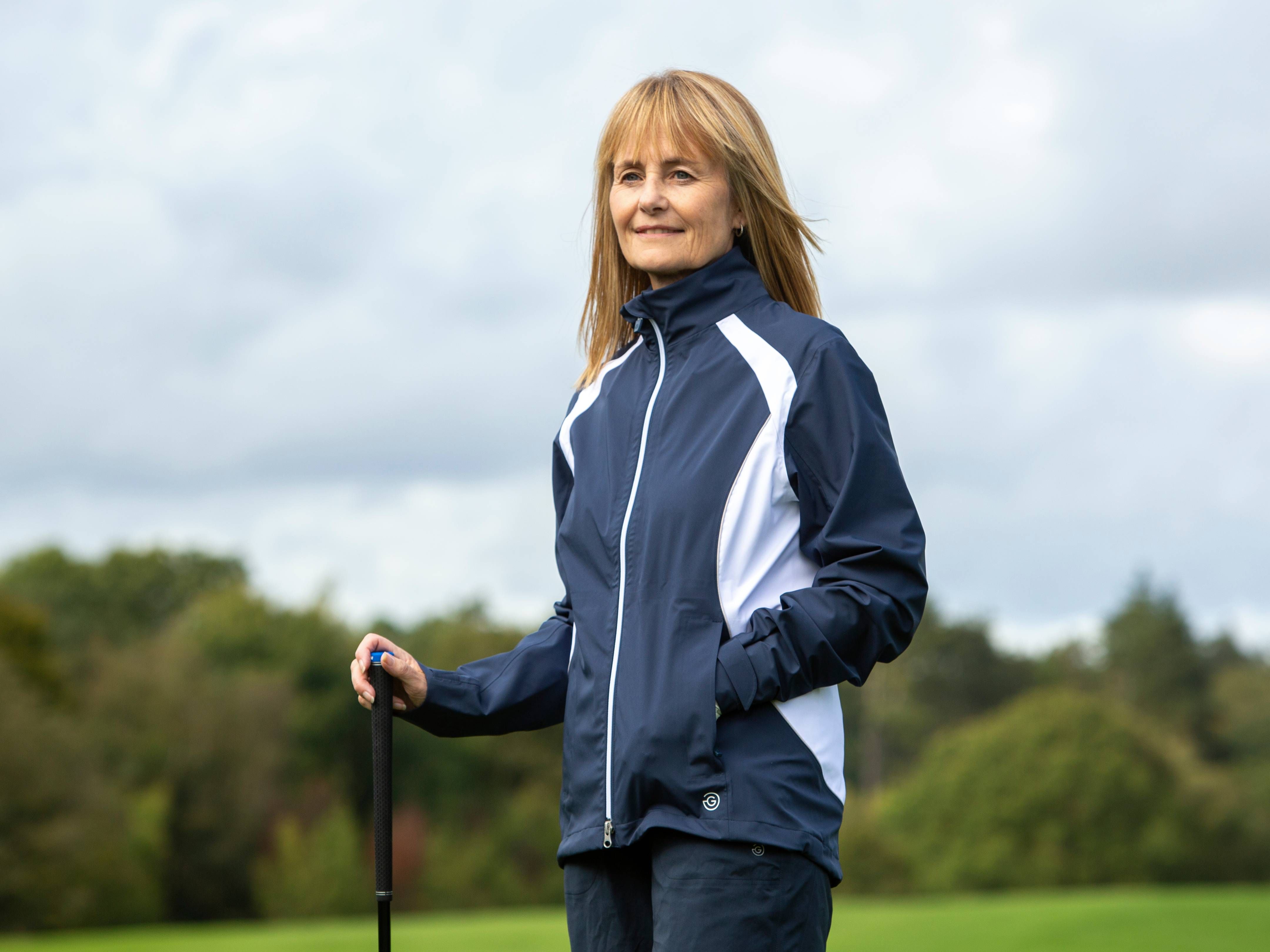 Professional female golfer wearing waterproof rain jacket on golf course