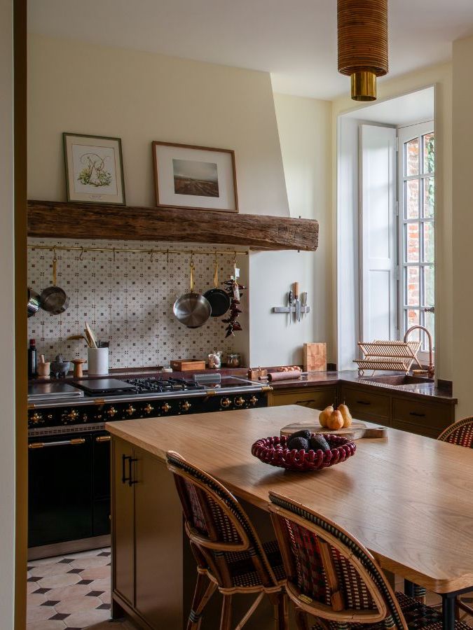 A country kitchen with deep red lower cabinets, and a large wooden dining table in the centre.