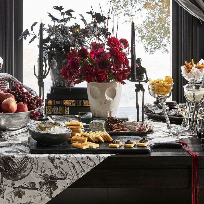 Halloween table with black and white toile runner, chrome serveware, and skull-shaped vases