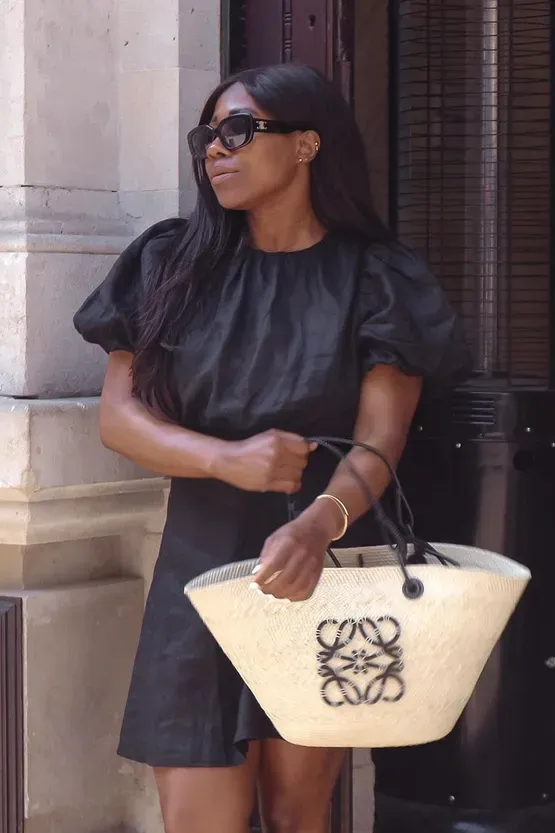 Woman wears Celine sunglasses, black dress and carries Loewe Anagram basket bag