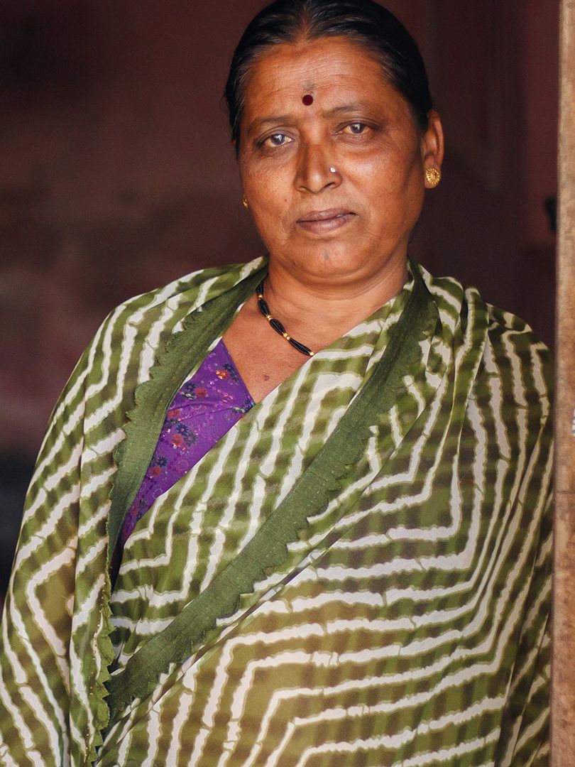 A woman in a green and white striped sari stands next to an open doorway.