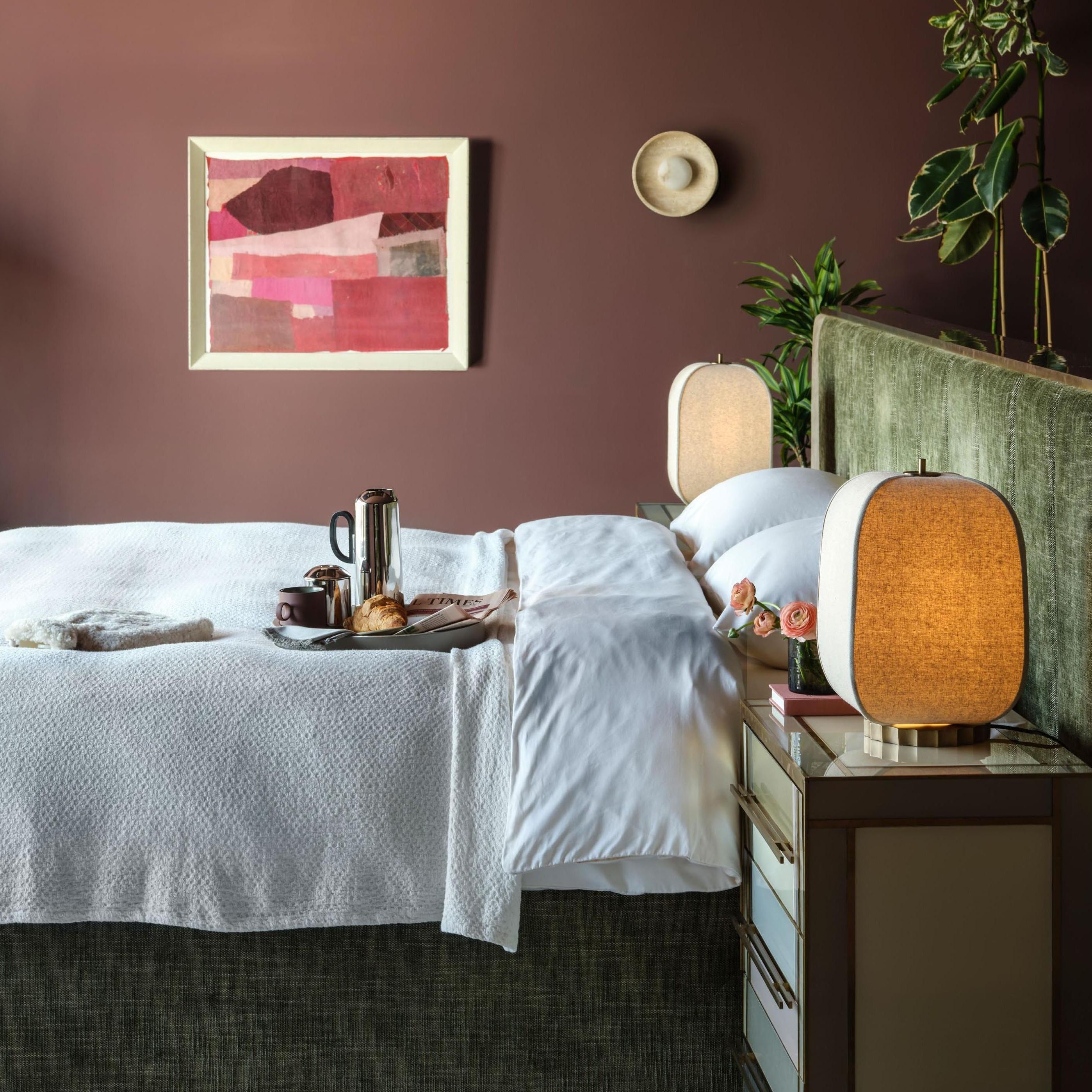 A modern luxe bedroom scheme with rich walls, a dark green headboard and large lamps