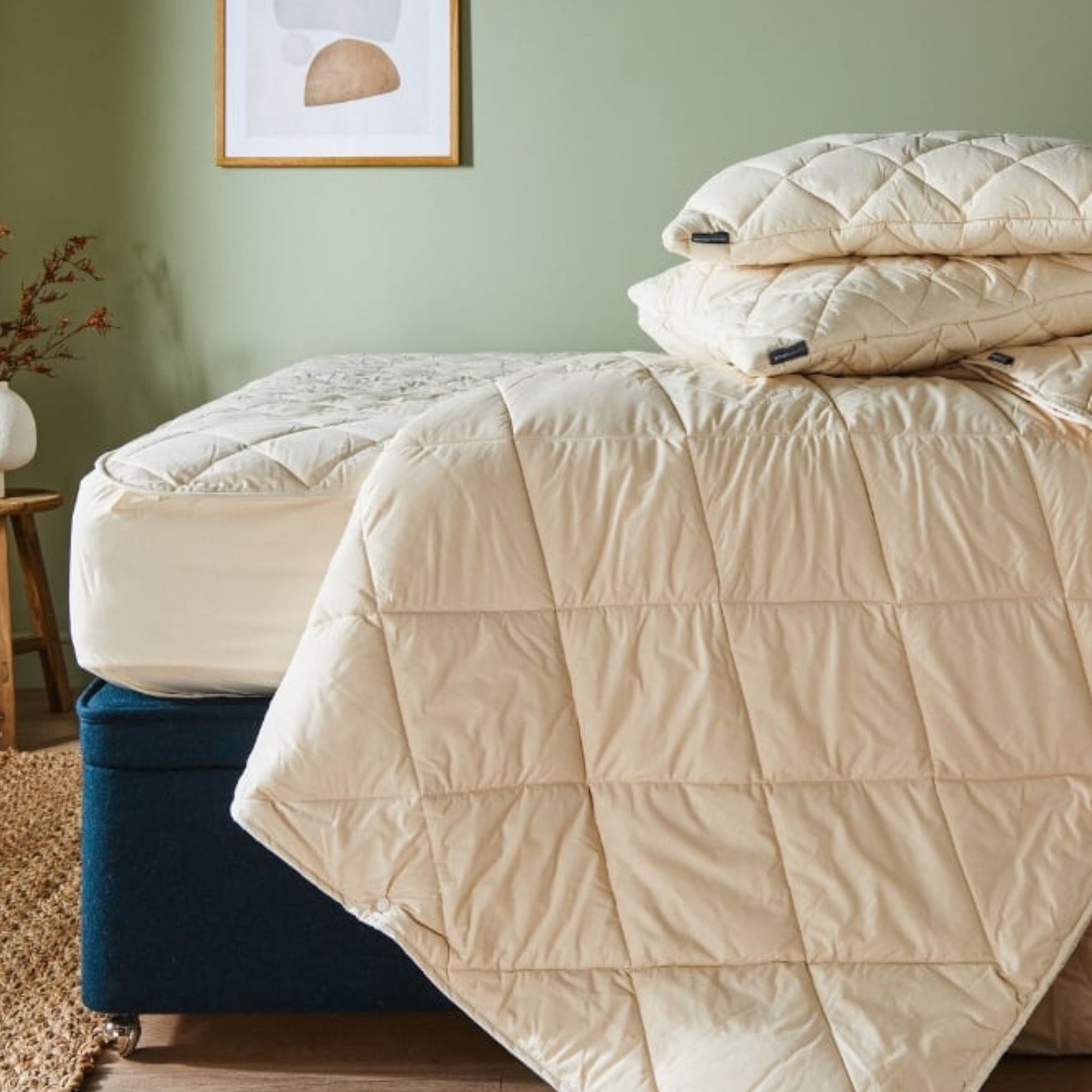 Woolroom Organic Washable Wool Comforter and pillows on a mattress against a green wall.