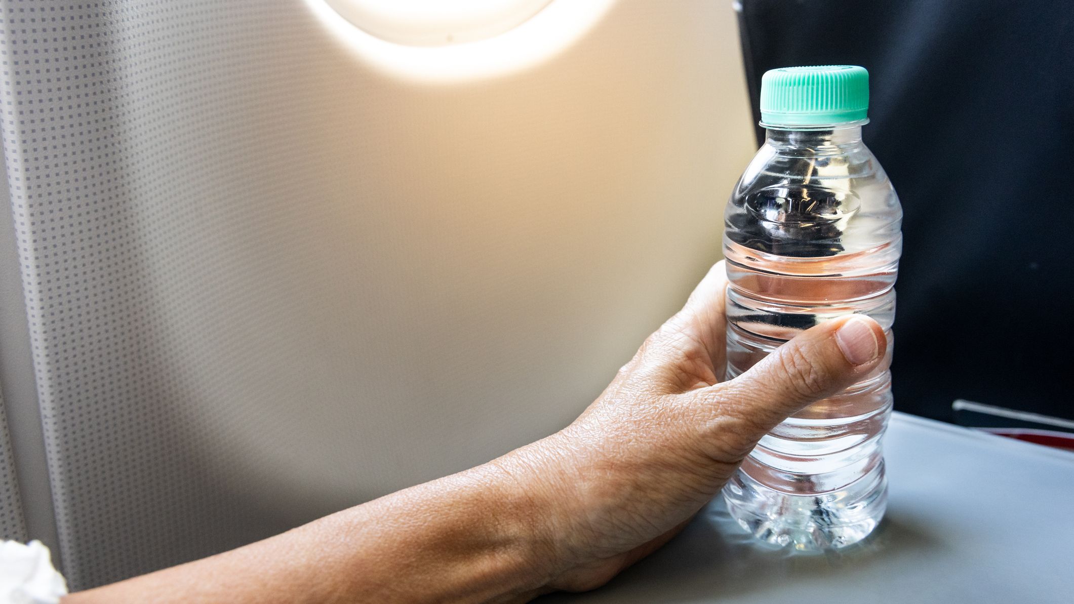 A hand holding a bottle of water on an airplane tray table