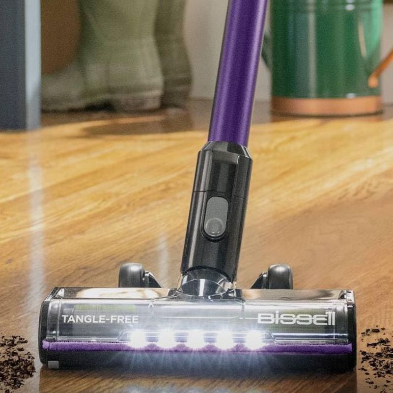 Bissell CleanView XR Pet 300W Stick cordless vacuum vacuuming mud from wooden floor with wellington boots, watering can and person&#039;s feet in background