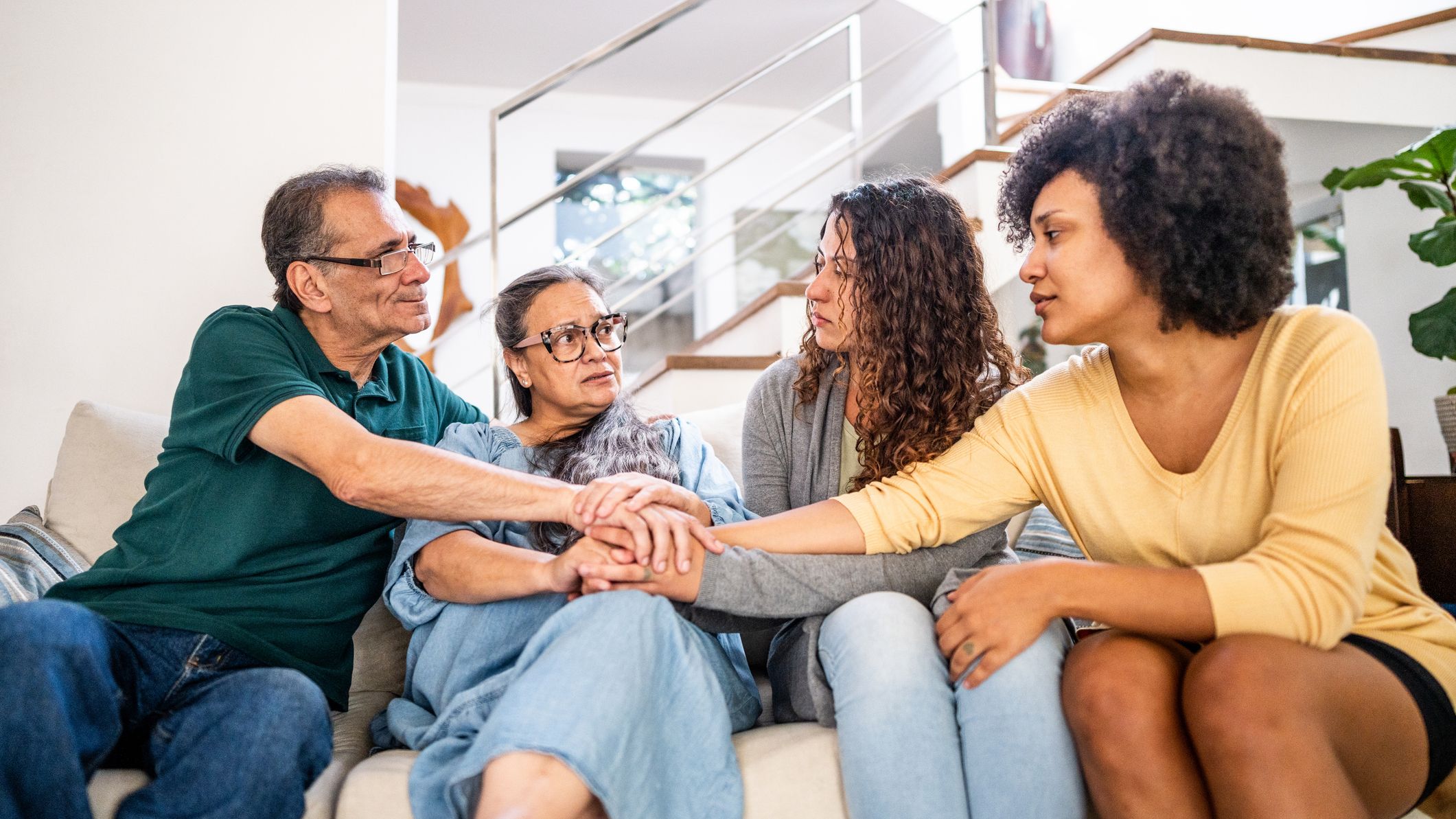 Young woman with her wife being comforted by her parents sitting on sofa in the living room at home