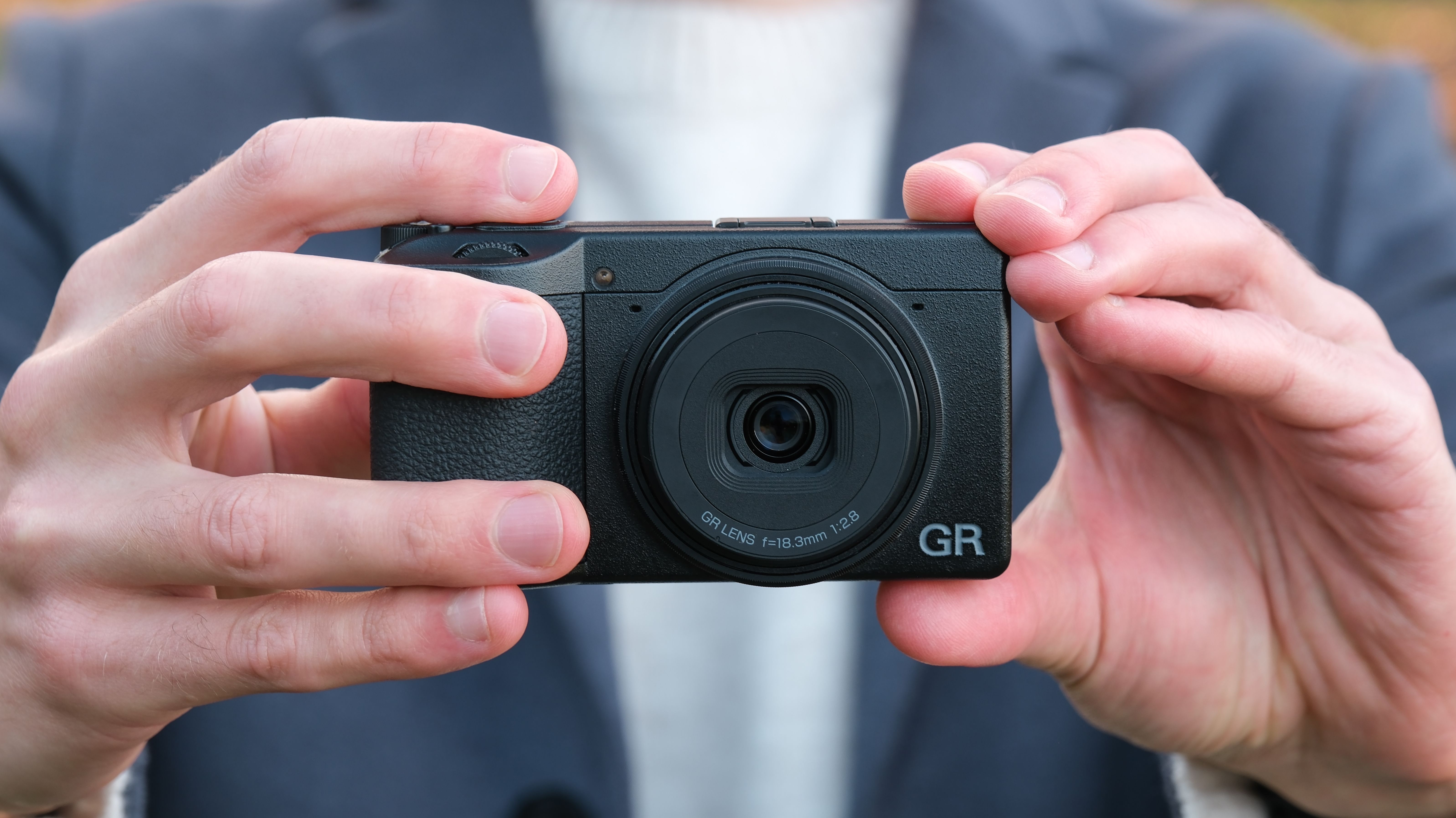 Ricoh GR IV compact camera held in a pair of hands