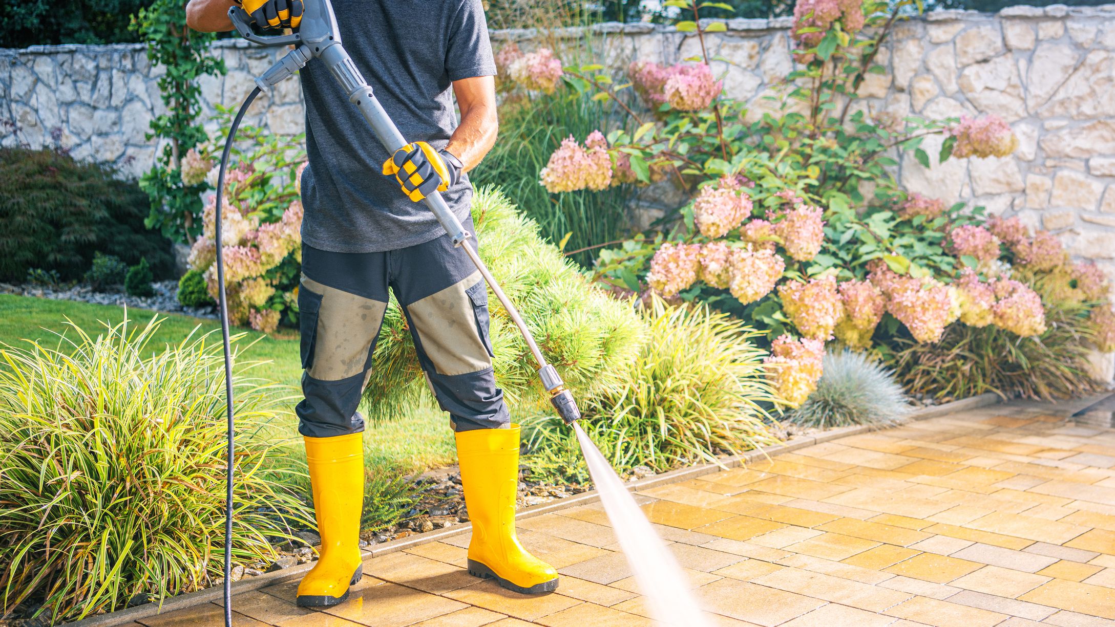 Man Using Pressure Washer to Clean Patio in Garden