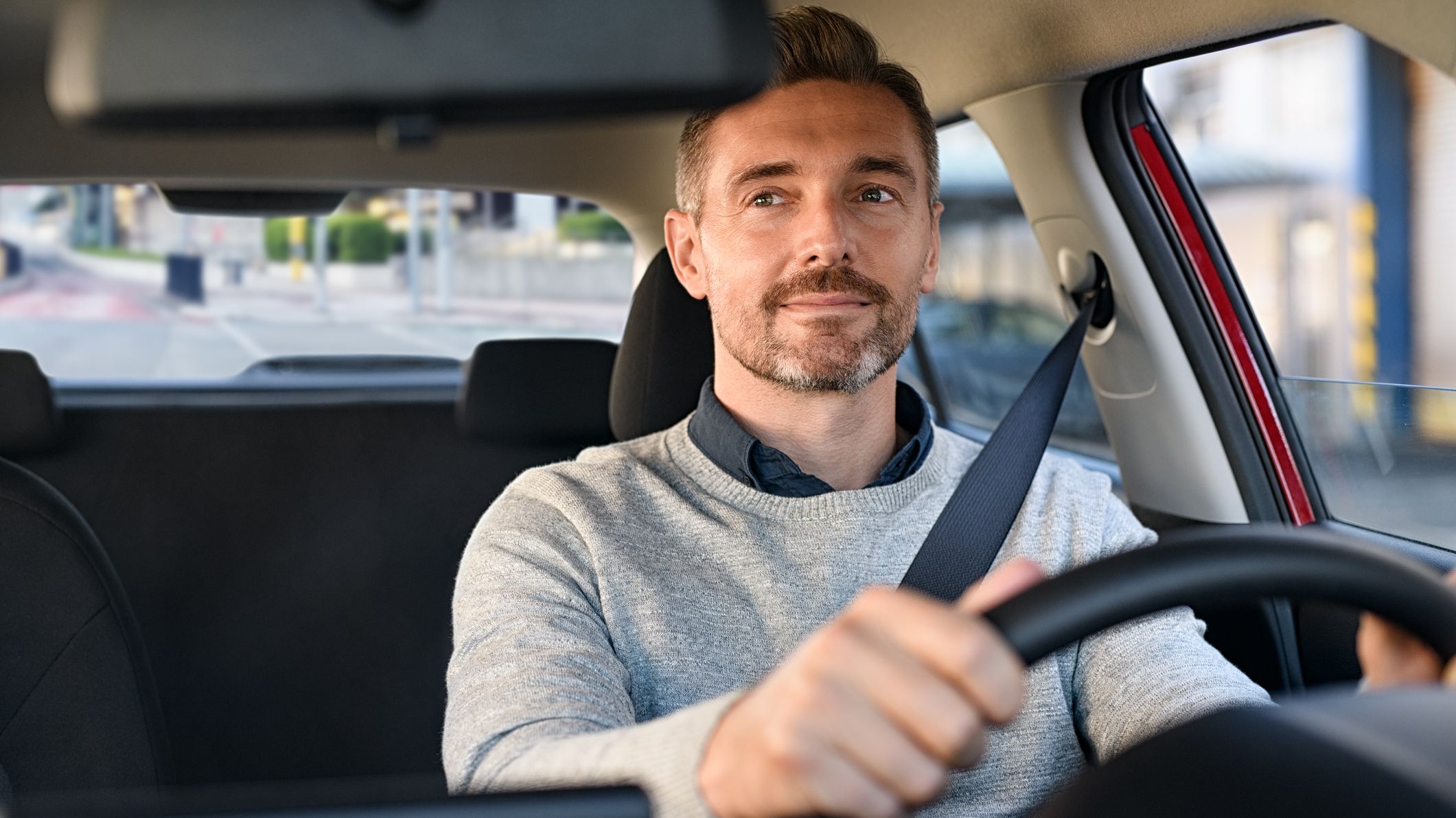 Smiling mature businessman with seat belt on driving vehicle