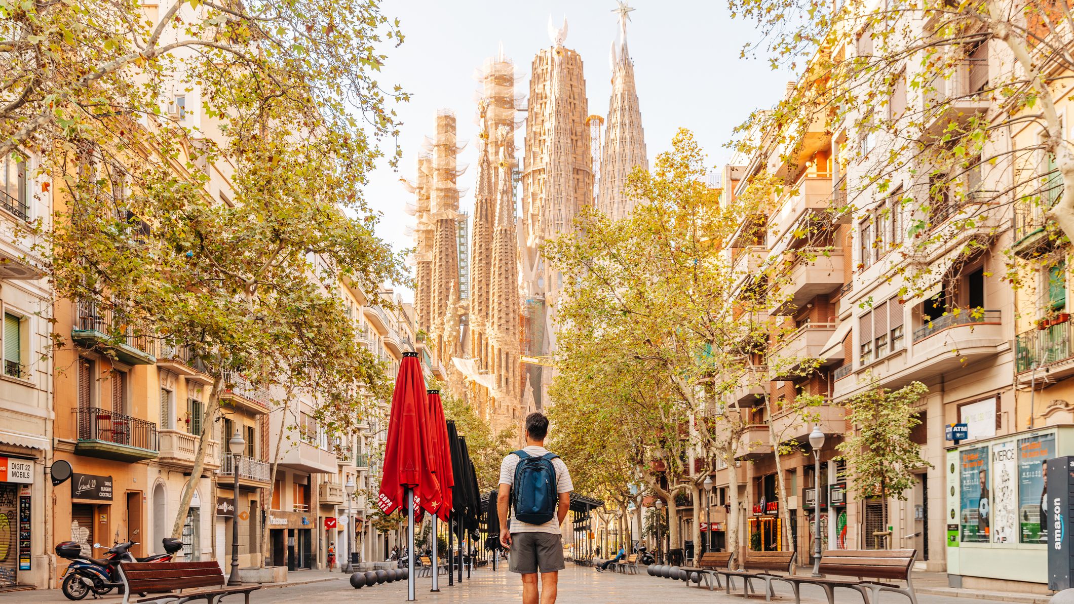 A man walks on an empty street in Barcelona towards the Sagrada Familia on a sunny day.