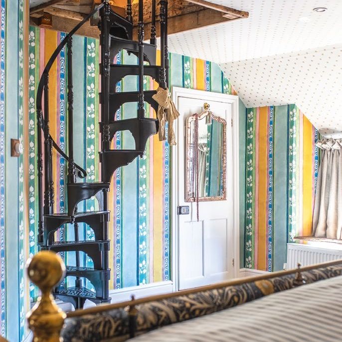 Bedroom with striped patterned walls and patterned ceiling. Iron spiral staircase going up into loft hatch.