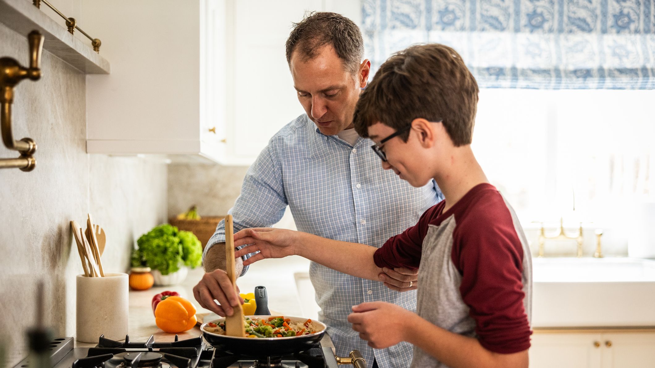 A father and son cooking eggs together in the kitchen.