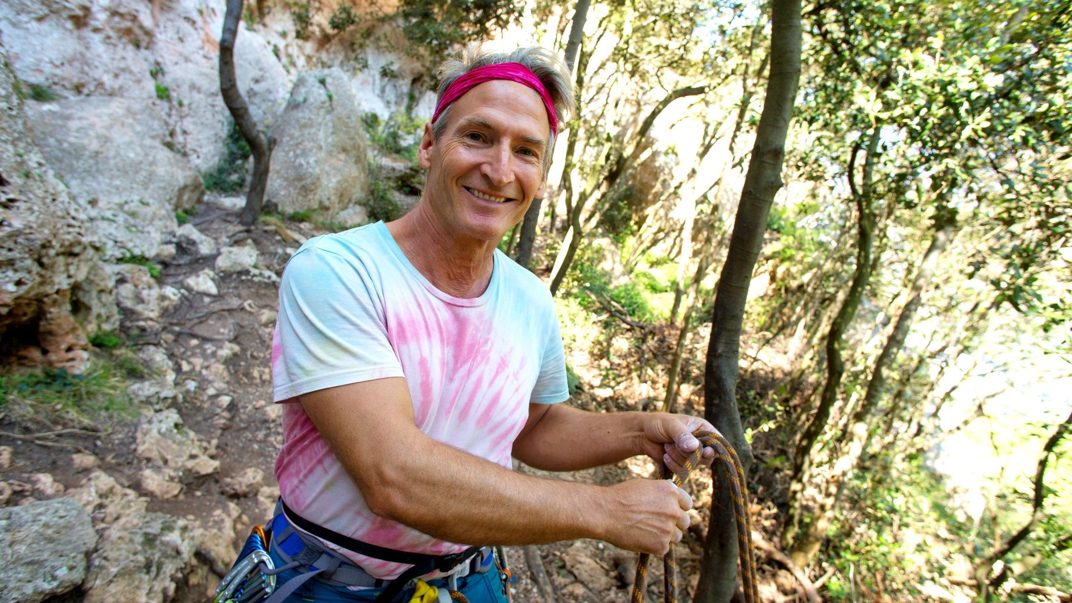 A fit, middle-aged man smiles as he pauses before technical rock climbing.